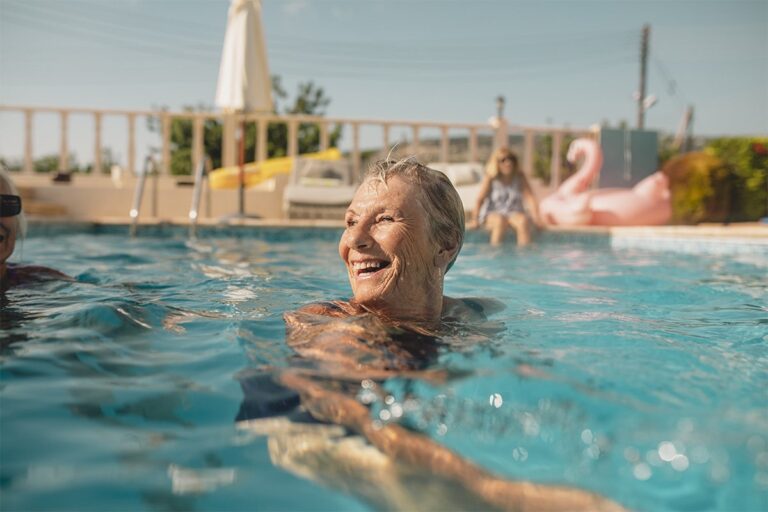 An older woman swimming in a pool and smiling.