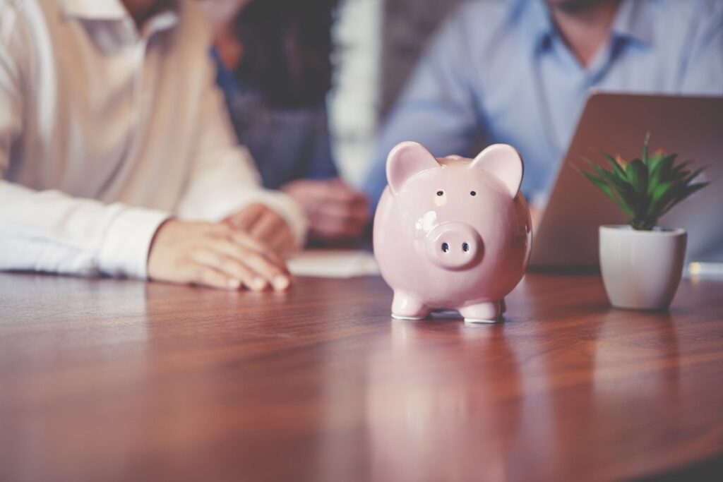 A pink piggy bank on a table with a couple in the background working on a computer.