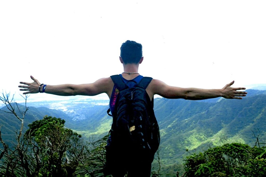Young man standing on the top of a mountain looking out with his arms stretched out.
